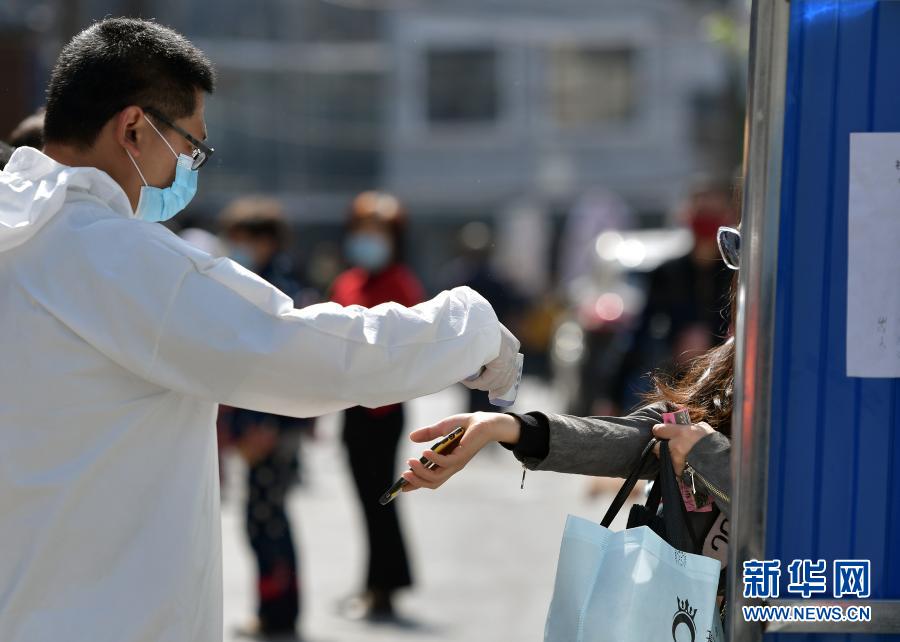 4月15日,值守在湖北武汉市武昌楚材社区出入卡口的工作人员为出入者测体温。新华社记者 李贺 摄